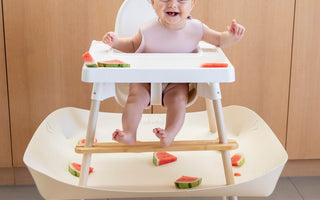 Baby eating watermelon in high chair with mess-catching tray, food-safe and easy clean design