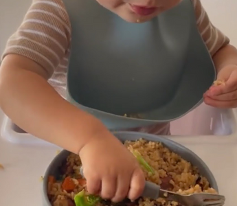 Toddler eating rice and veggies with bib, mess-free mealtime solution