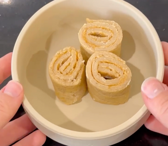 Hands holding a bowl with three rolled-up peanut butter and banana snacks, ideal for mess-free meals.