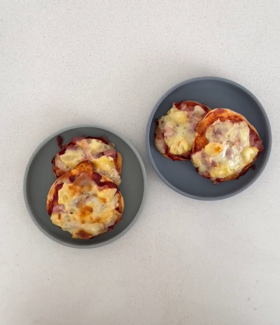 Two gray plates with mini cheesy pizzas on a clean countertop, perfect for mess-free meals.