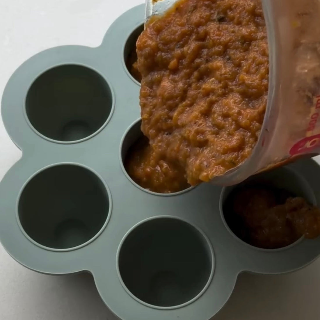 Pouring baby food puree into silicone storage cups for easy meal prep and freezing.