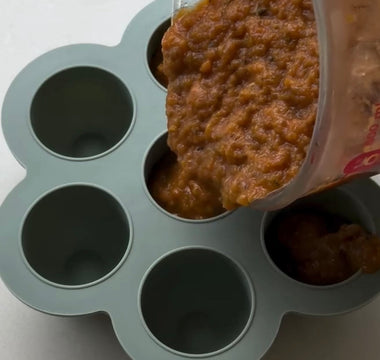 Pouring baby food puree into silicone storage cups for easy meal prep and freezing.