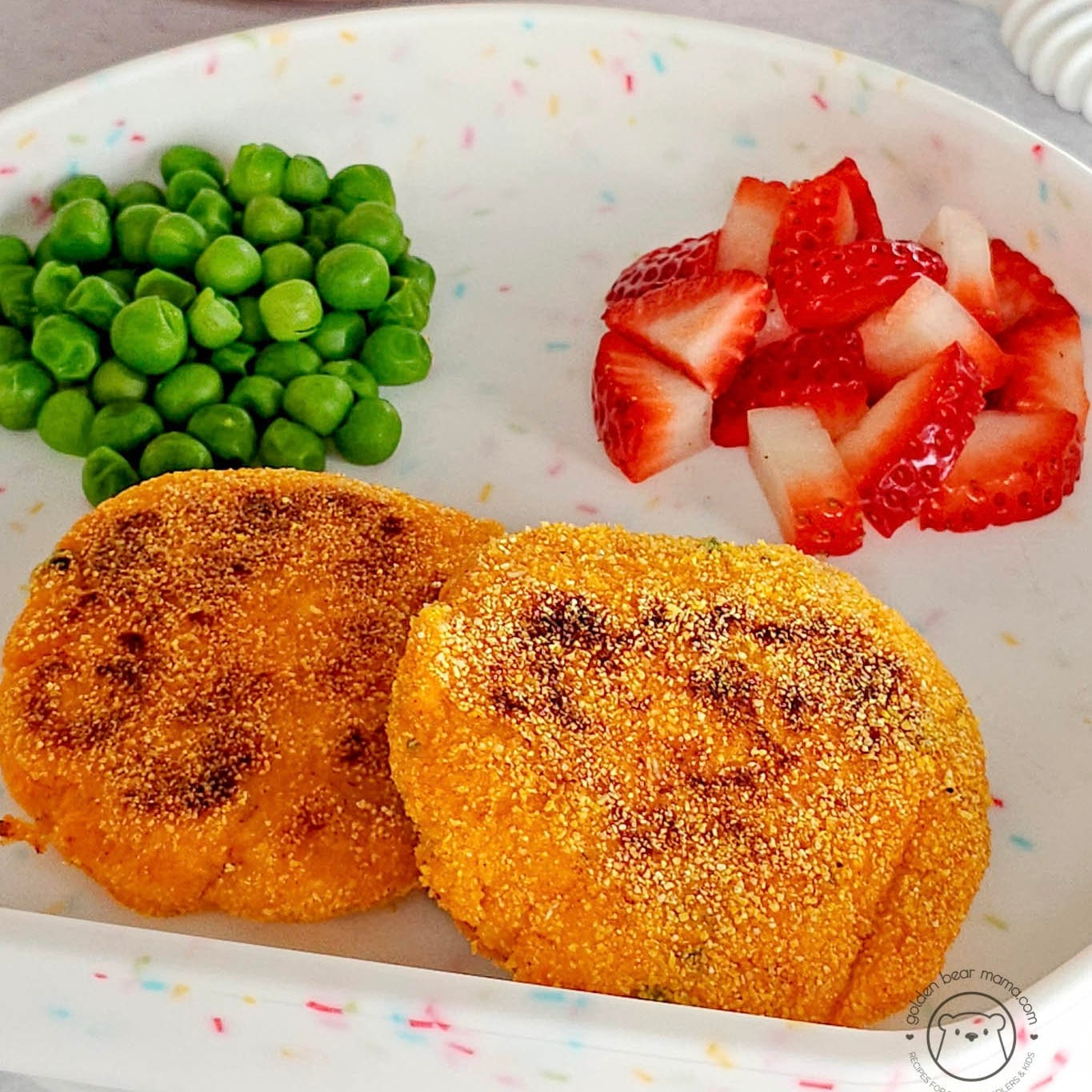 Kid-friendly meal with crispy patties, peas, and strawberries on colorful plate